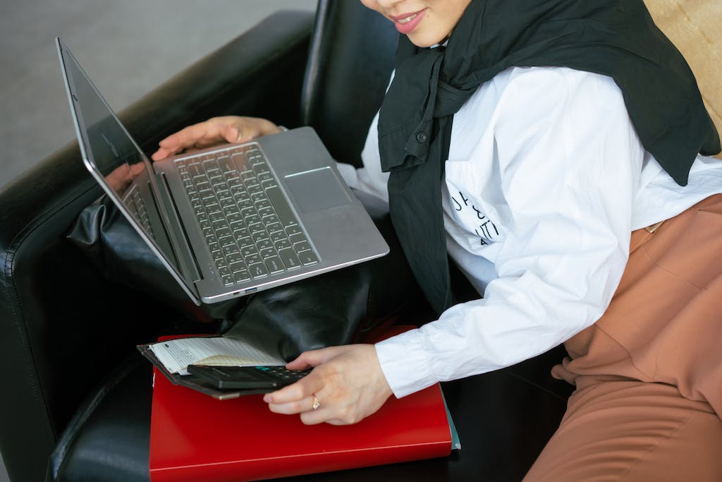 Woman Lying on the Sofa and Using a Laptop and a Calculator